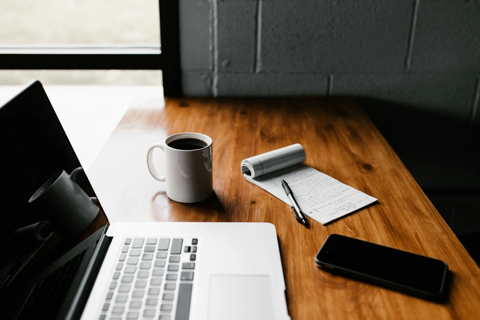 A clean wooden desk with laptop, coffee, and a handwritten notepad