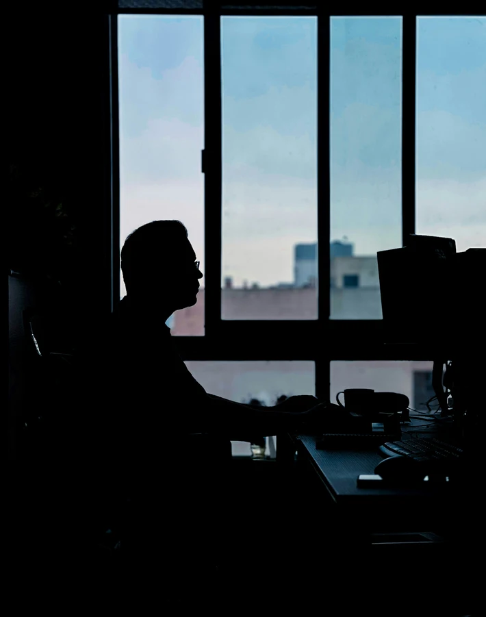 Silhouette of a developer at a desk against a bright window with a city skyline